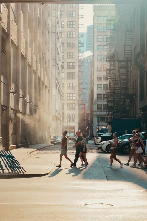 Free People walking through a sunlit alleyway between tall buildings, capturing urban life and architecture in warm light. Stock Photo