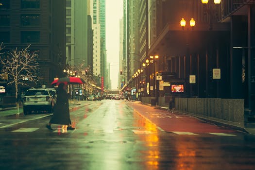 A pedestrian crosses a wet city street holding a red umbrella, reflecting urban lights.