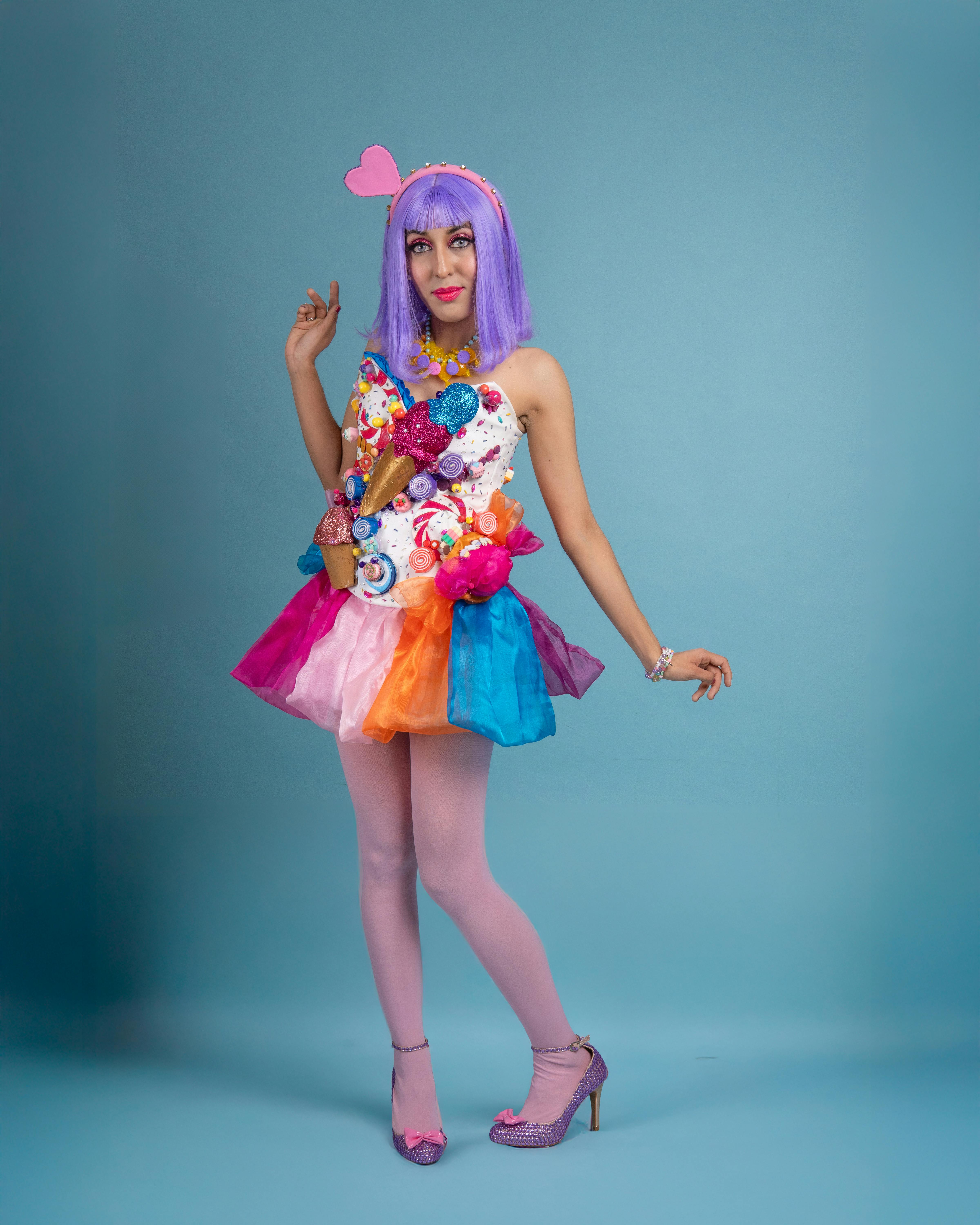 A young woman in a vibrant cosplay outfit poses against a blue background.