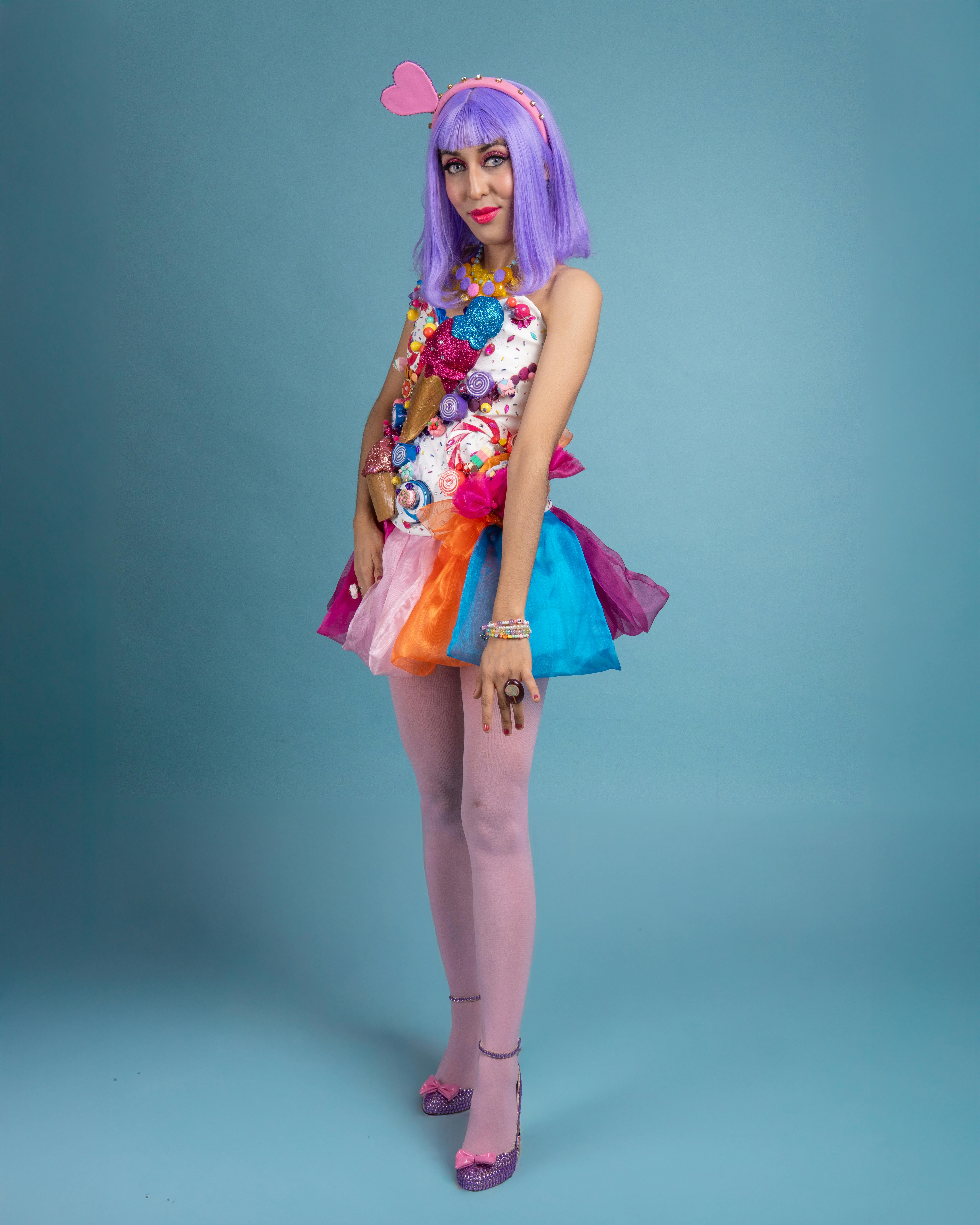 ingyenes Egy fiatal nő színes cosplayben, lila parókával és kreatív jelmeztel, kék háttér előtt. Stockfotó