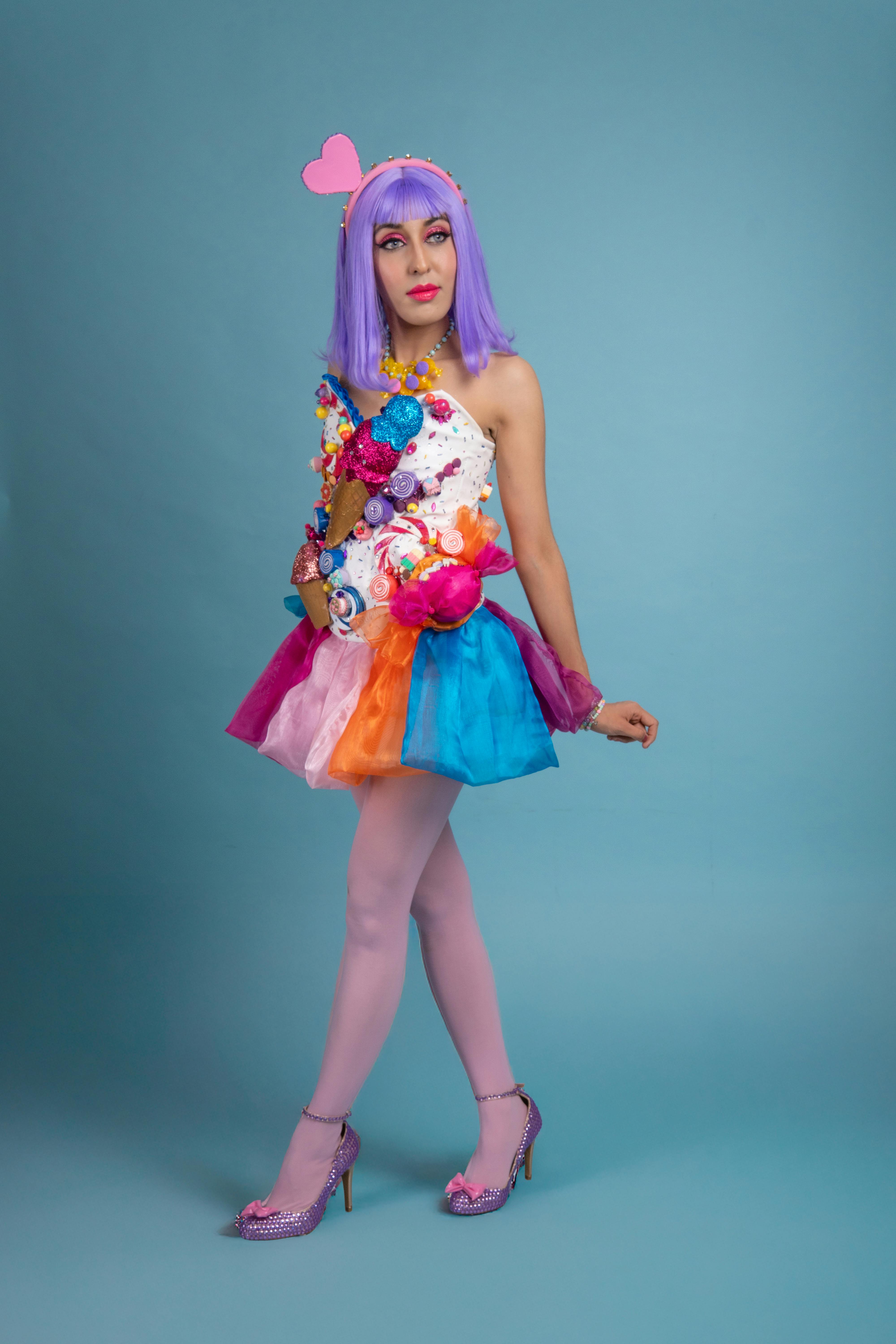 ingyenes Egy fiatal nő vibráló cosplayben, lila parókát és színes ruhát visel kék háttér előtt. Stockfotó