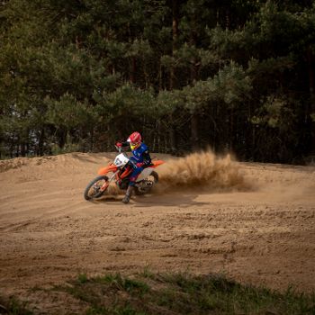 Exciting motocross action with a racer speeding through sand on a forest track.