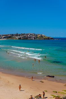 A vibrant day at Bondi Beach featuring swimmers and surfers under clear blue skies.