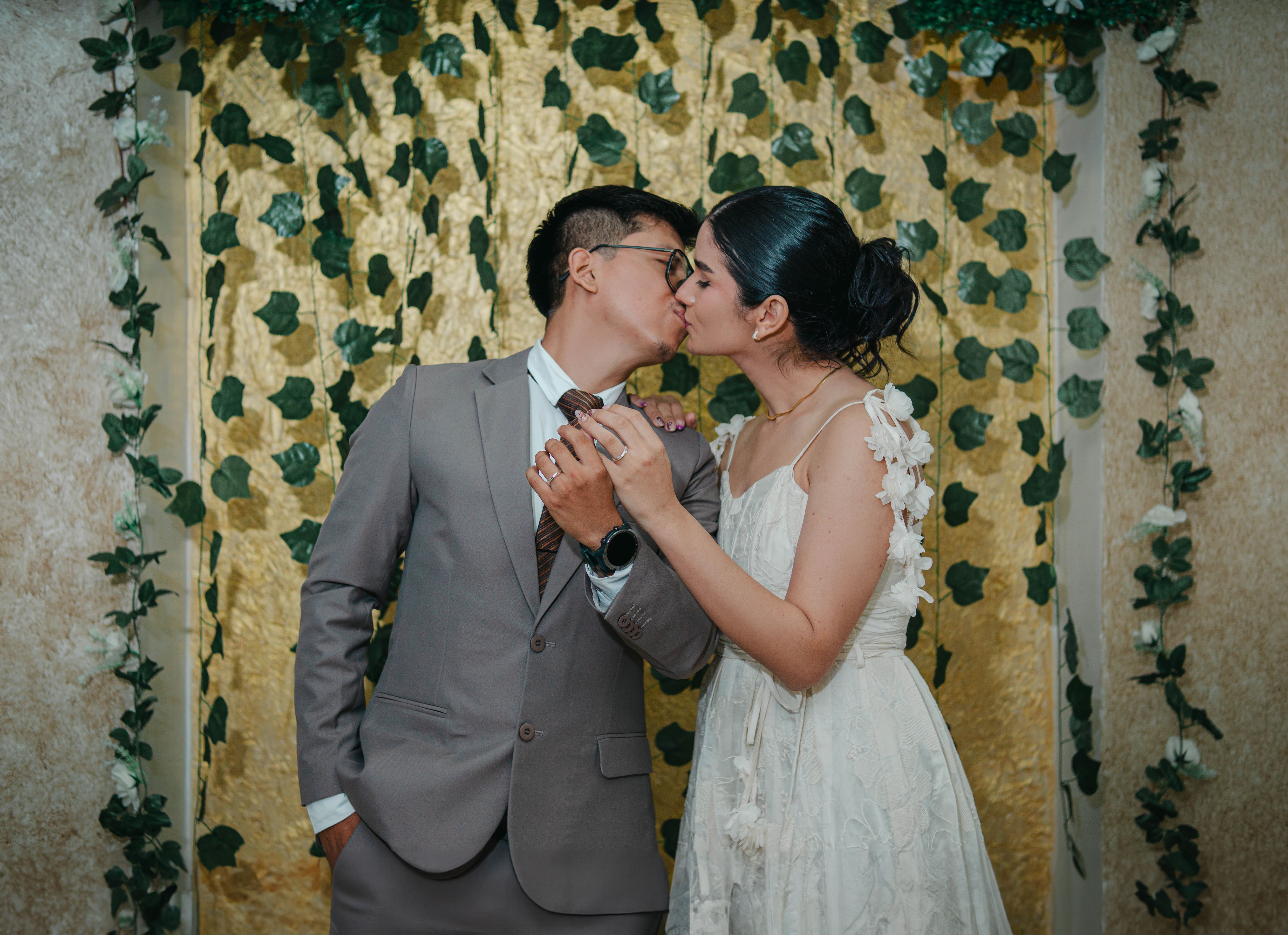 A wedding couple shares a tender kiss against a lush ivy backdrop, capturing love and elegance.