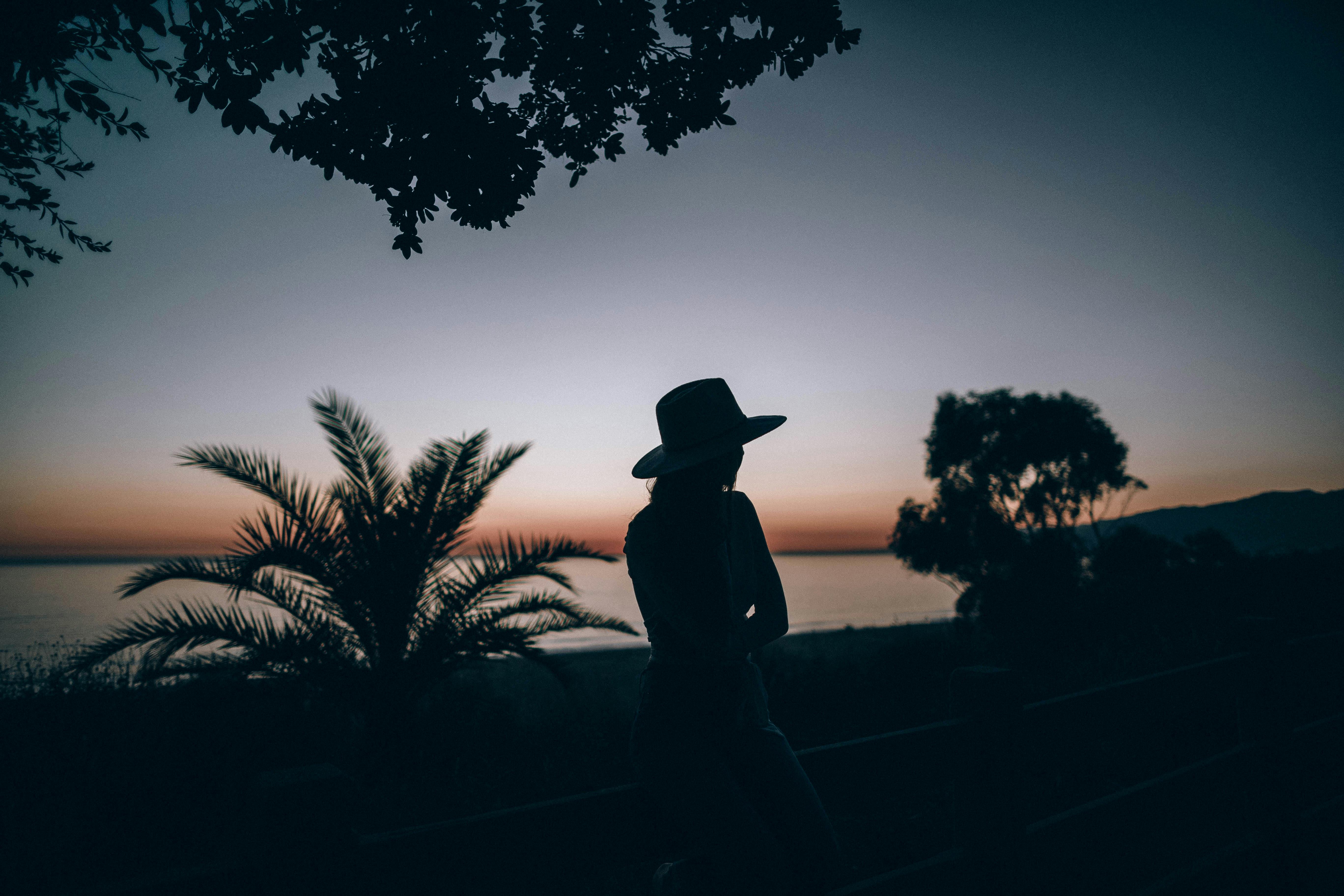 日落时分，海边一位戴帽子女人的剪影，捕捉到一种宁静而沉思的心情