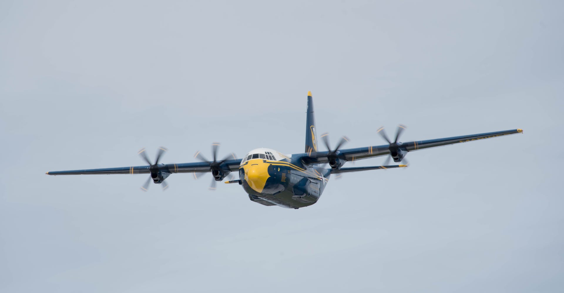 Front view of a military transport plane flying in clear sky, propellers spinning.