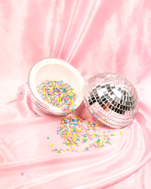 Vibrant confetti spills from a disco ball on a soft pink satin backdrop.