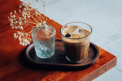 Free Glass of iced coffee with dried flowers on wooden tray, creating a cozy atmosphere. Stock Photo