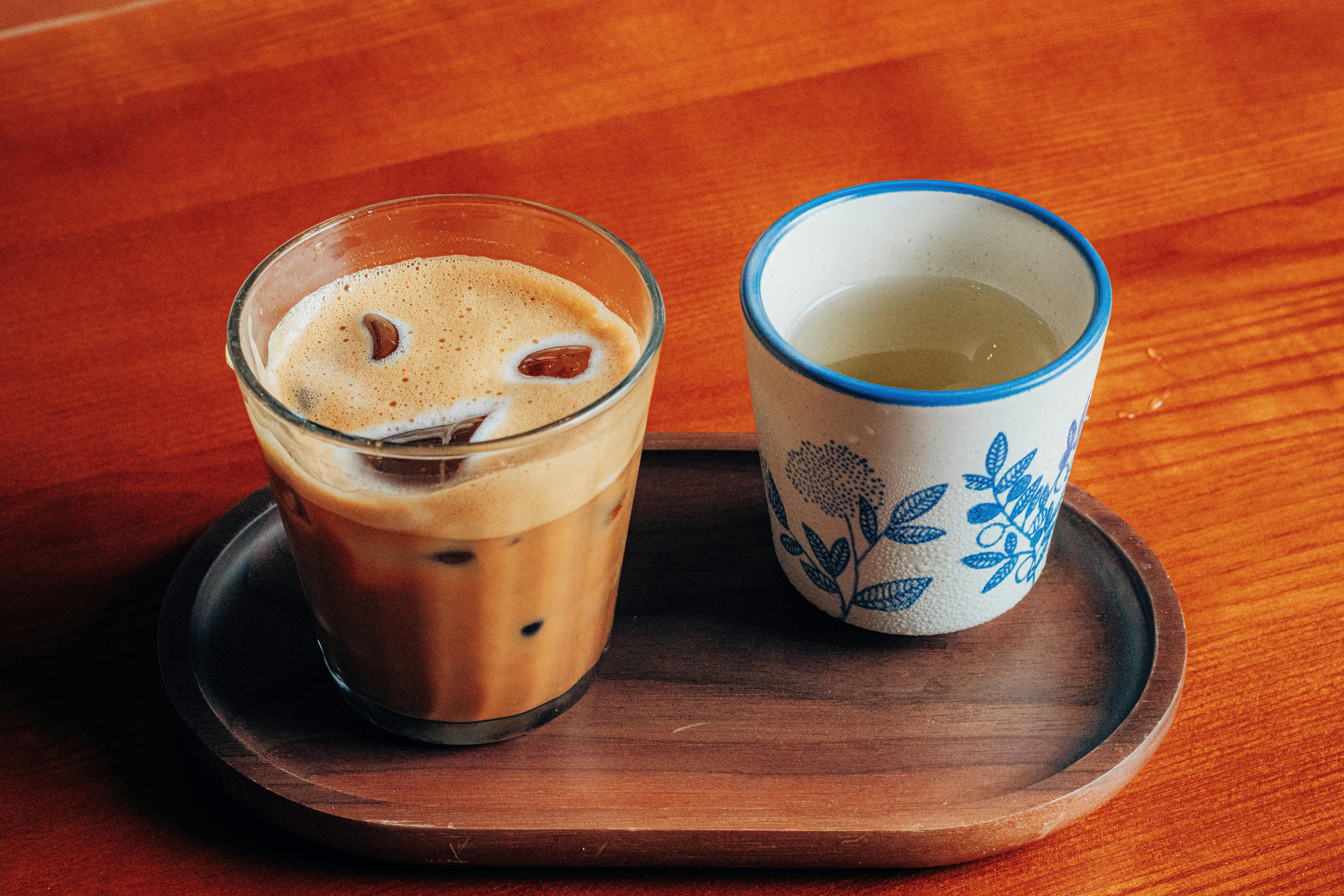 A refreshing iced coffee and herbal tea served on a wooden tray indoors.