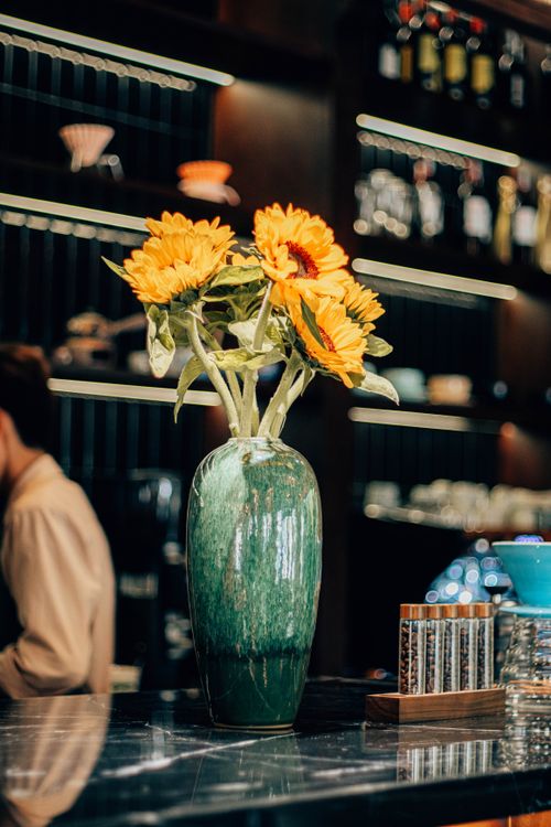 Free Sunflowers in a green vase on a stylish cafe counter with blurred background. Stock Photo