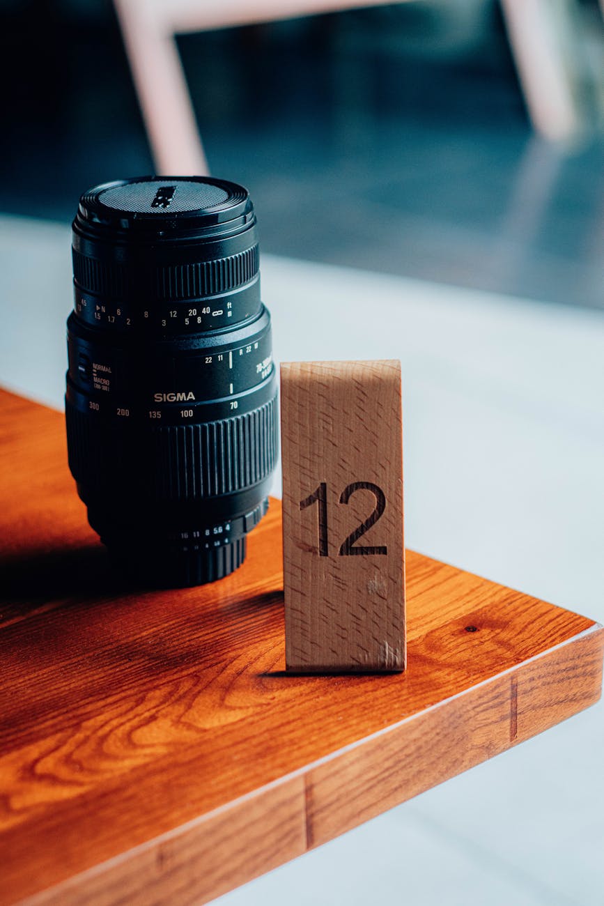Camera lens and wooden number block '12' on a stylish wooden table.