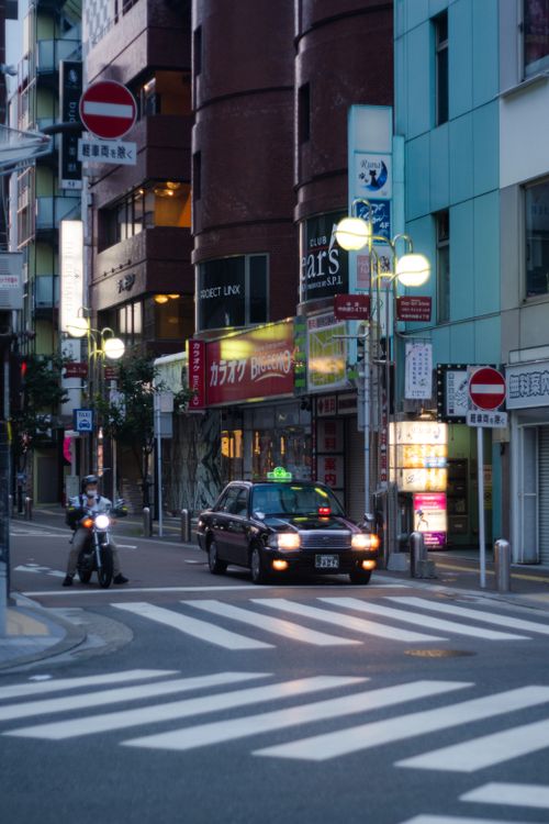 Free A bustling street in Fukuoka at night featuring a taxi and vibrant city lights. Stock Photo
