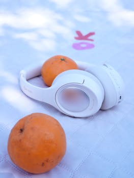 White headphones paired with oranges on a textured tablecloth, outdoors.