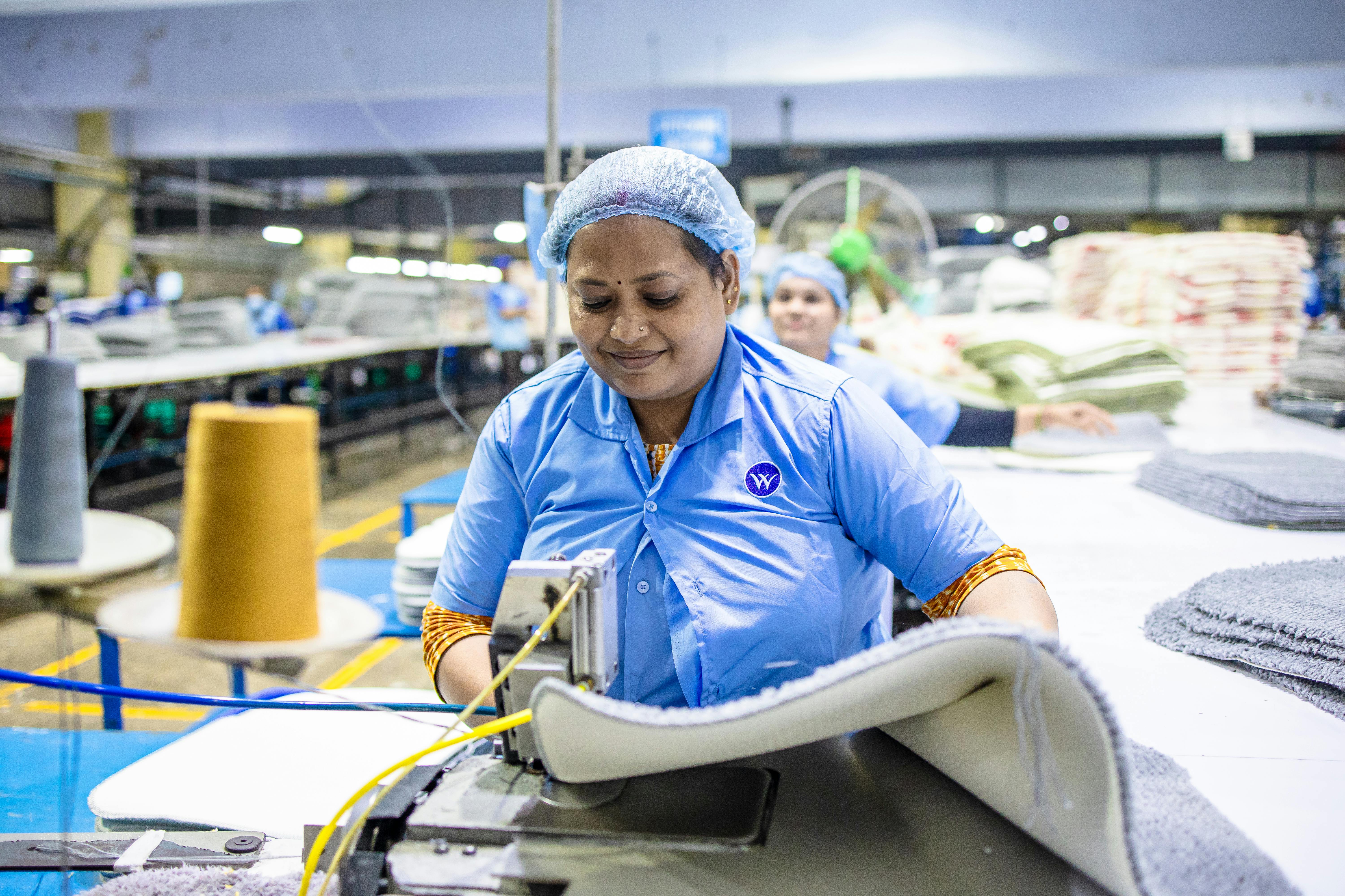 Factory worker operating a textile machine in a manufacturing facility while wearing a hairnet and uniform.