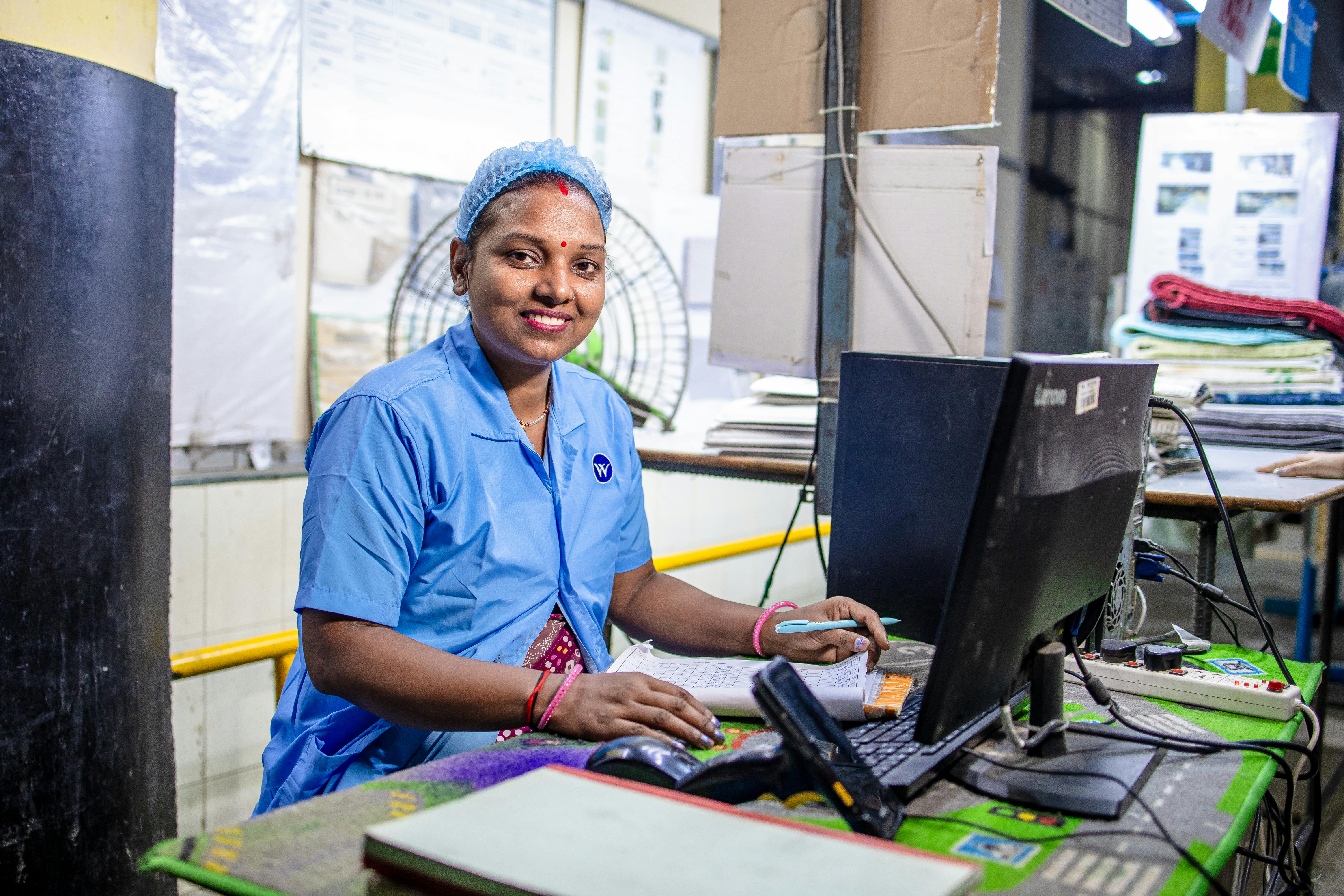 Smiling worker in blue uniform at desk in a textile factory, showcasing industry professionalism.