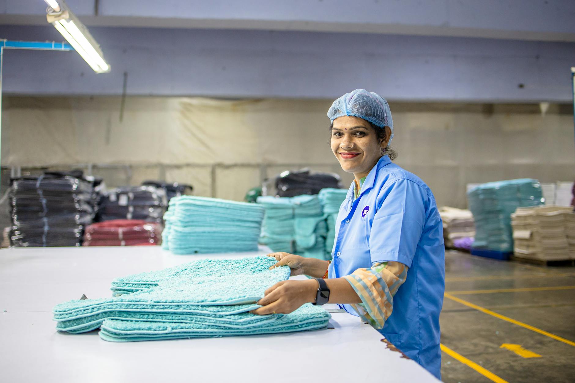 A cheerful factory worker organizes textile products on a table in a vibrant manufacturing setting.