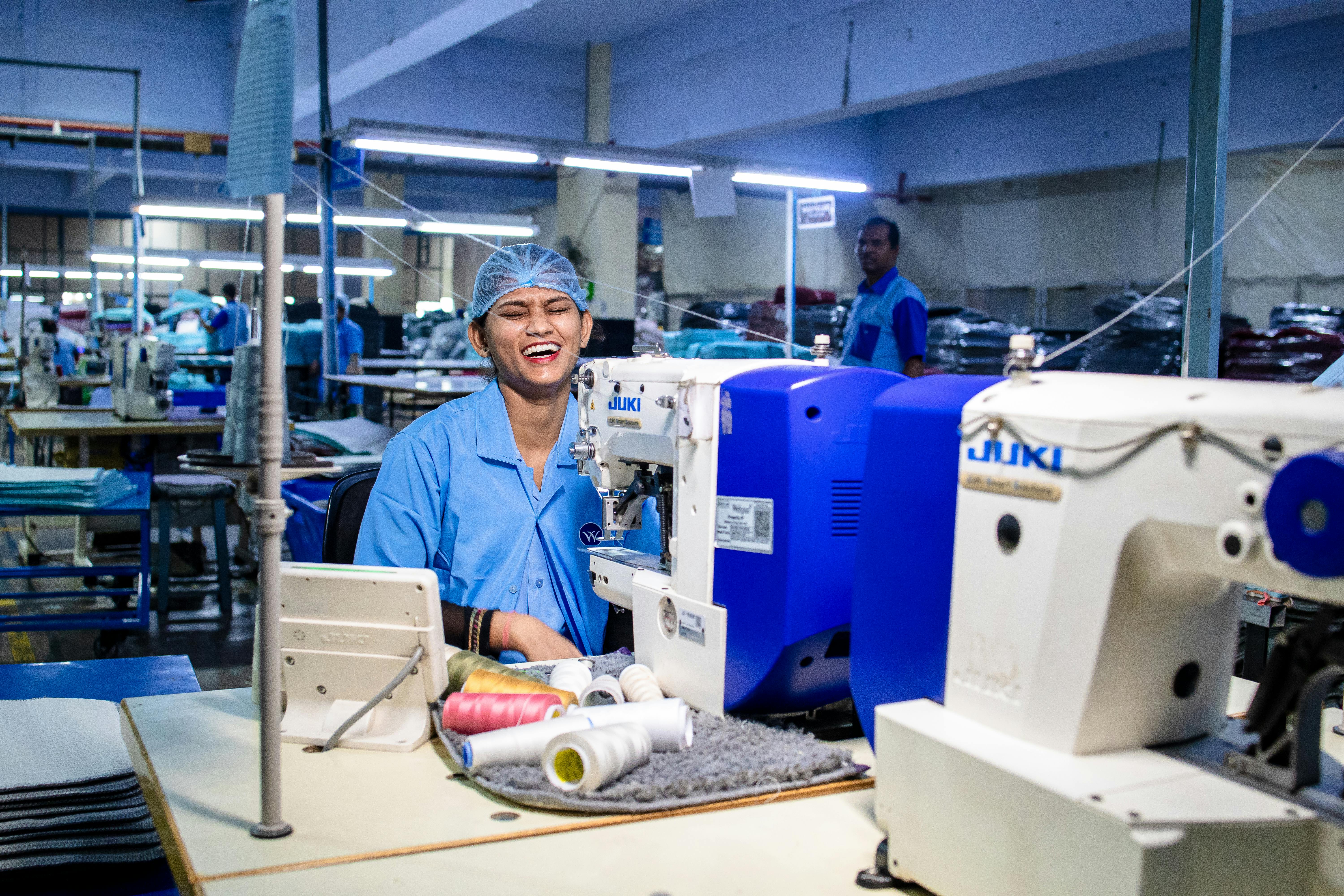 Cheerful textile worker sewing in a bustling factory environment.