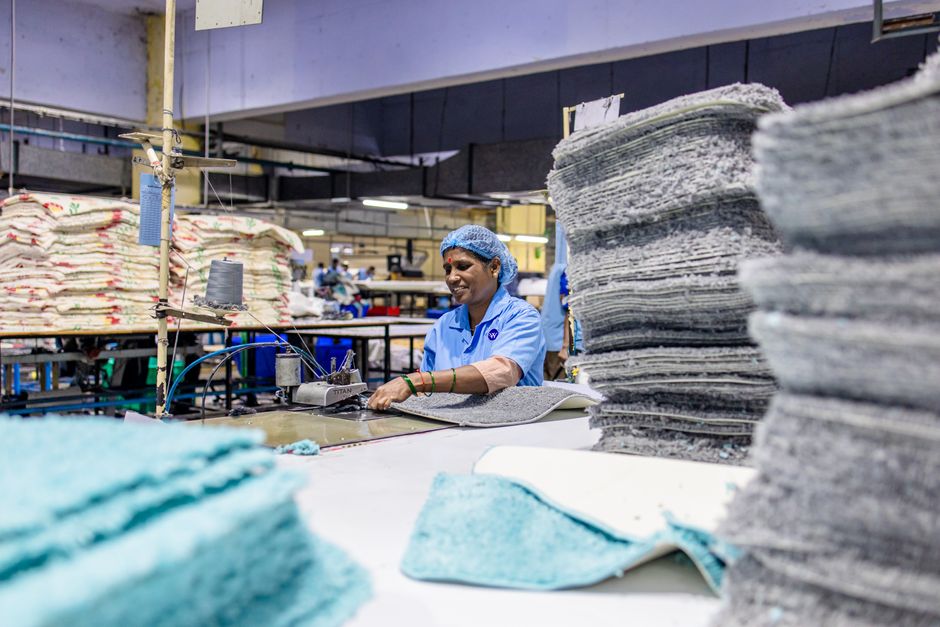 Female factory worker stitching textiles with machinery in a busy production facility.
