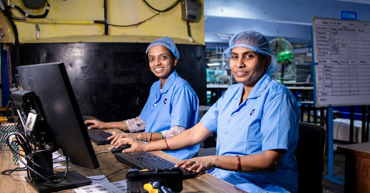 Two female workers at a textile factory operating computers in an industrial setting.