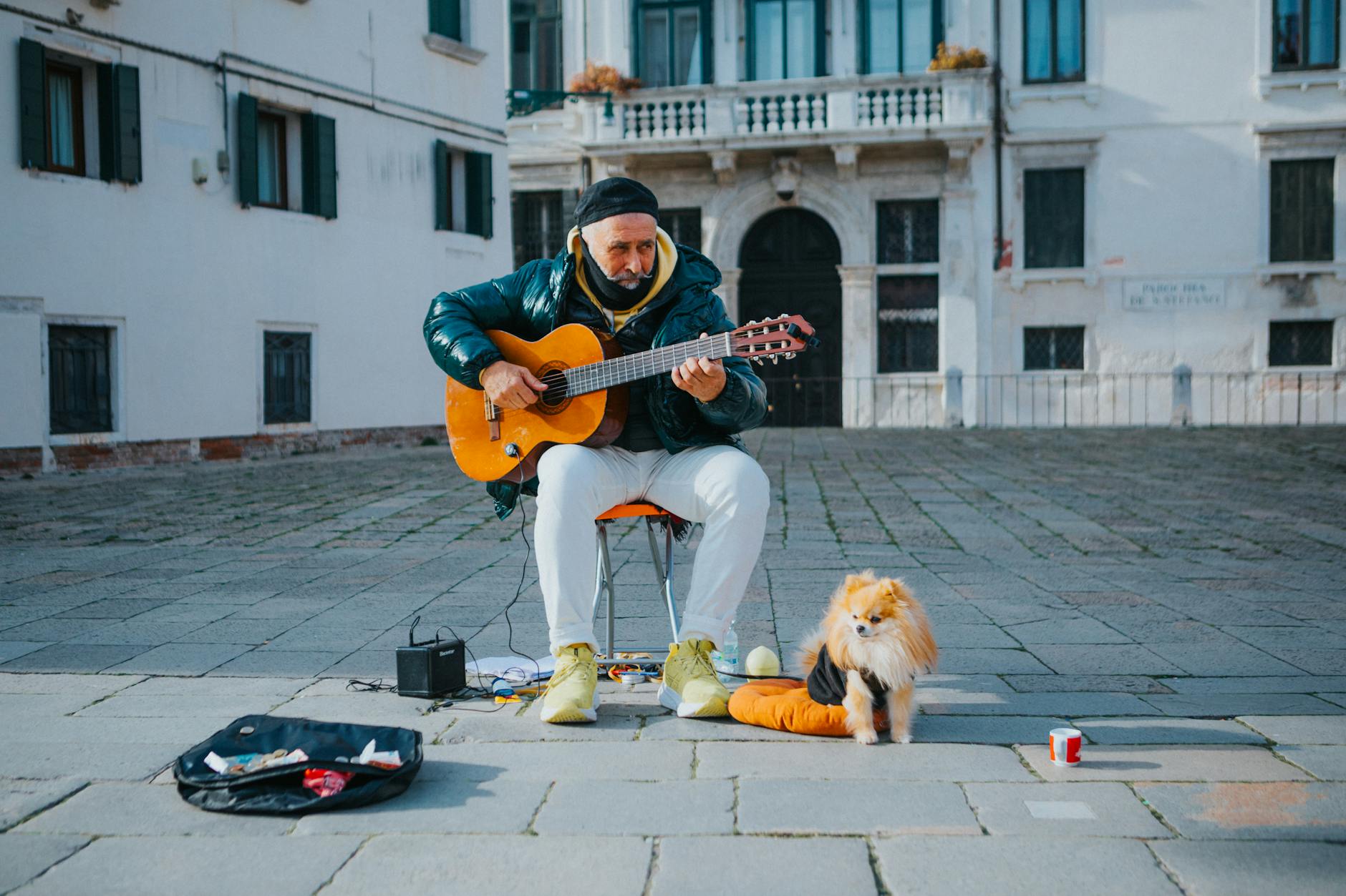 Street musician playing guitar with his dog beside him in an urban setting, crea