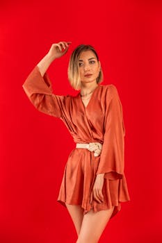 Stylish portrait of a woman in a red dress standing against a vibrant red background.