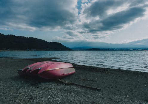 A tranquil scene with a pink kayak on the shore of Lake Kawaguchi, with mountains in the background.