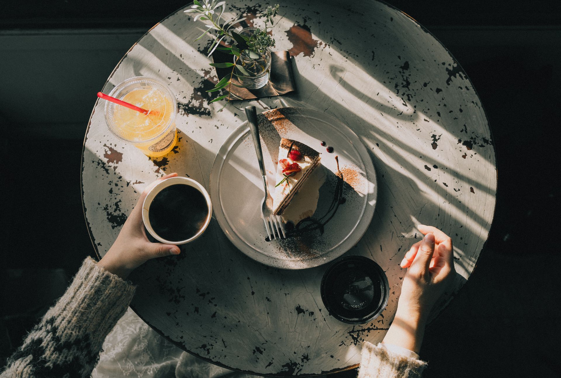 Overhead view of a cozy café table with a slice of cake, coffee, and juice, bathed in warm afternoon light.
