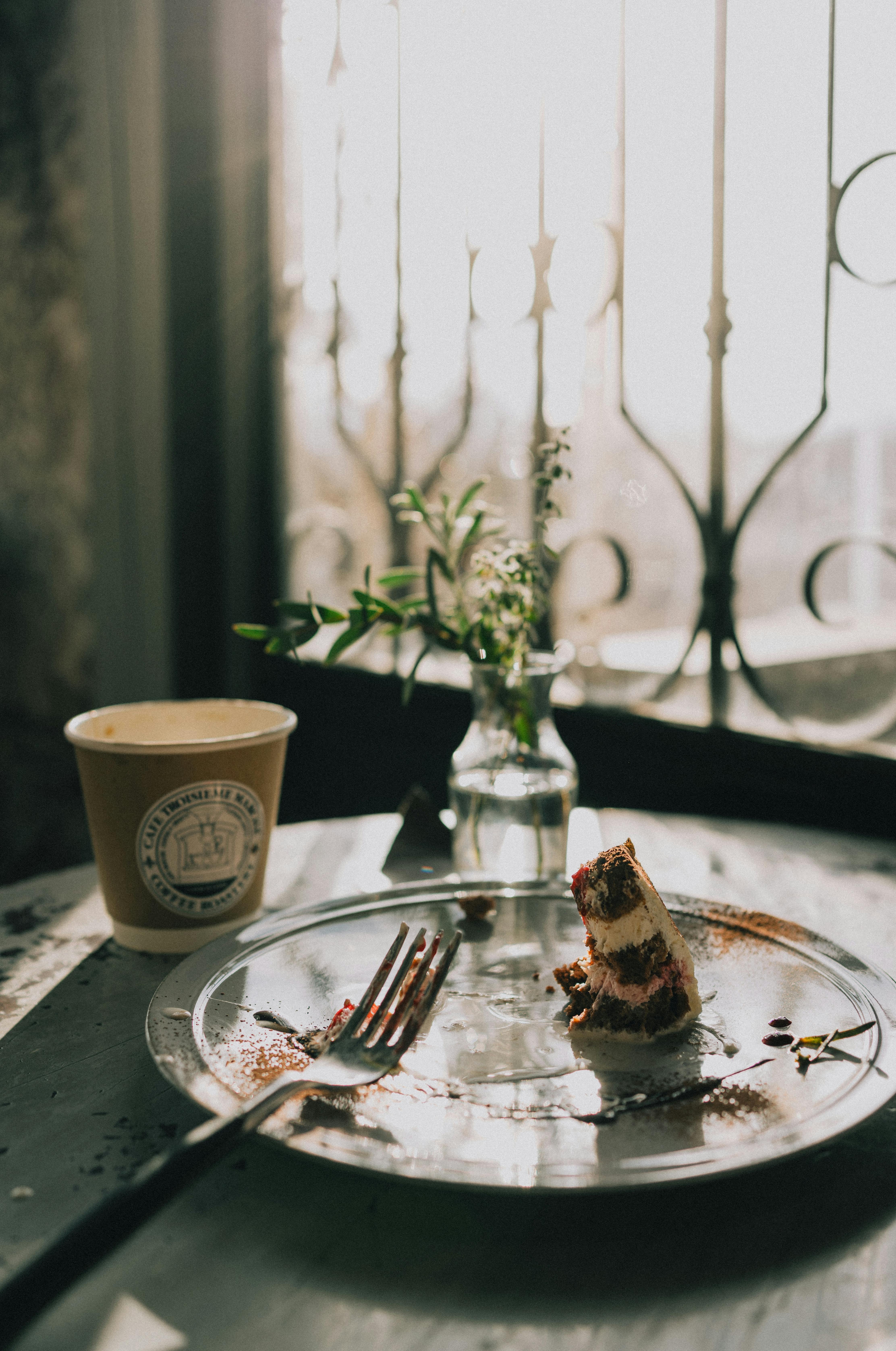 A serene moment with a slice of cake, coffee, and flowers at a rustic café by the window.
