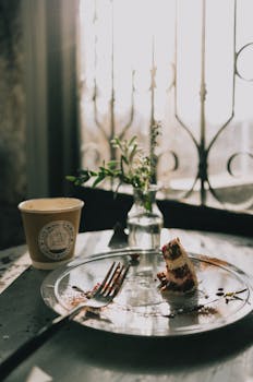 A serene moment with a slice of cake, coffee, and flowers at a rustic café by the window.