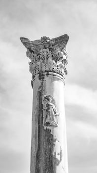 Black and white image of a Corinthian column with an ornate capital against the sky.