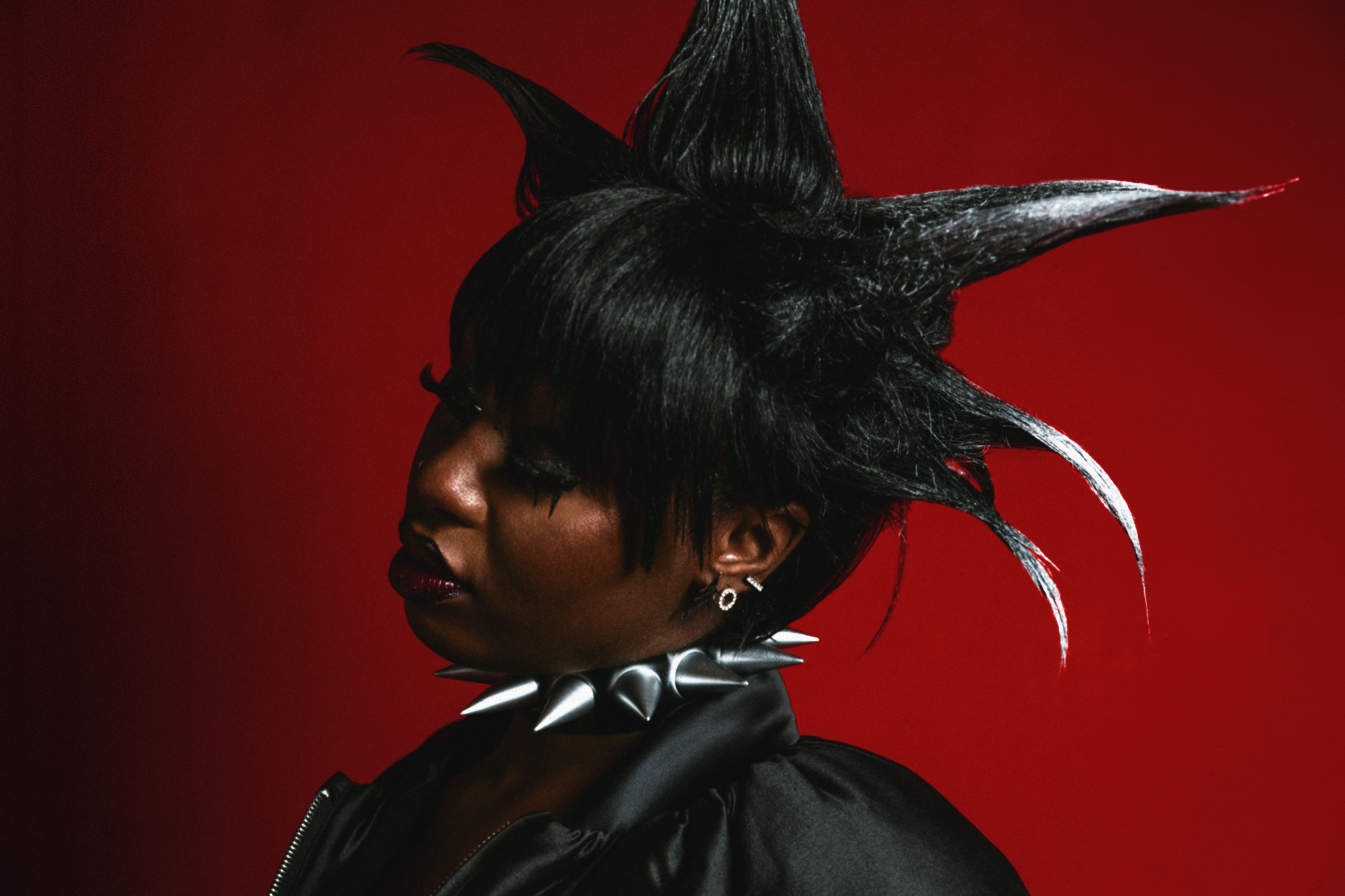 Portrait of a woman with spiky hair and spiked choker on a red background.