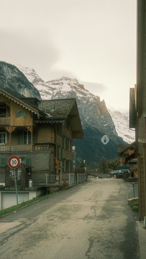 Free Scenic street in an Alpine village with traditional wooden houses and snowy mountains. Stock Photo