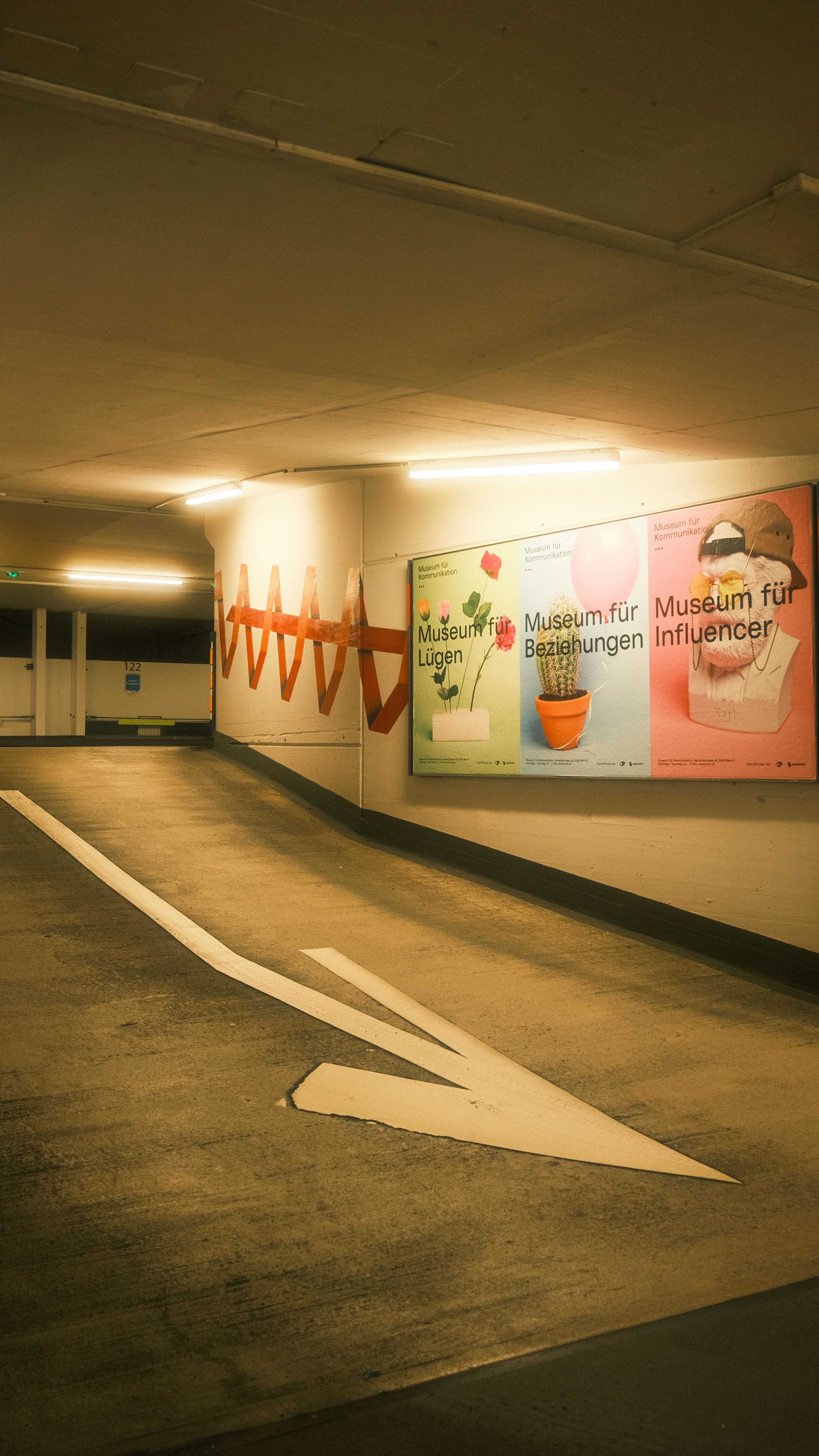 Kostenlos Ein schwach beleuchtetes Parkhaus mit bunten Museumswerbeplakaten an der Wand. Stock-Foto