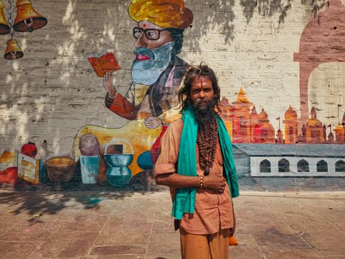Free Sadhu standing before a colorful street art mural in Varanasi, India. Stock Photo