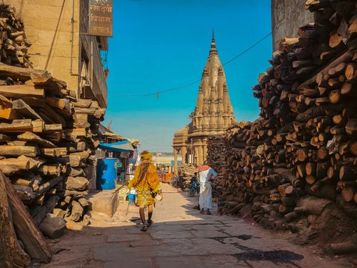 Free Street scene in Varanasi with wood piles and temple in view, showcasing daily life. Stock Photo