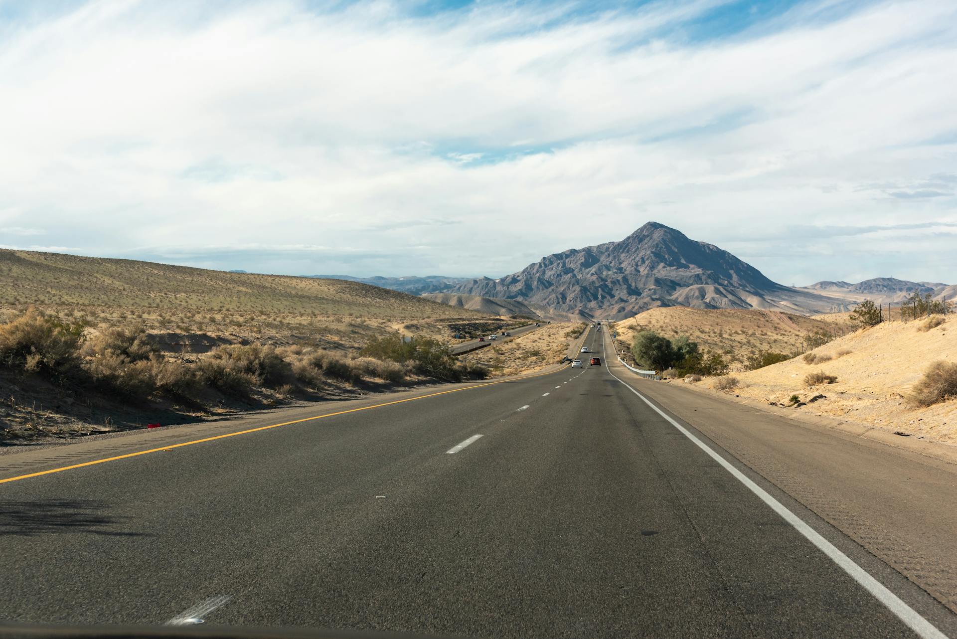 Scenic view of a desert highway in California leading towards a distant mountain range under a clear sky.