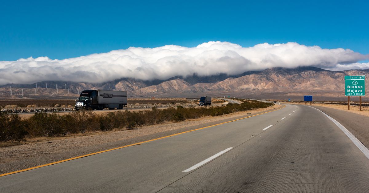 A scenic highway view with trucks, mountains, and clouds in California's Mojave Desert.