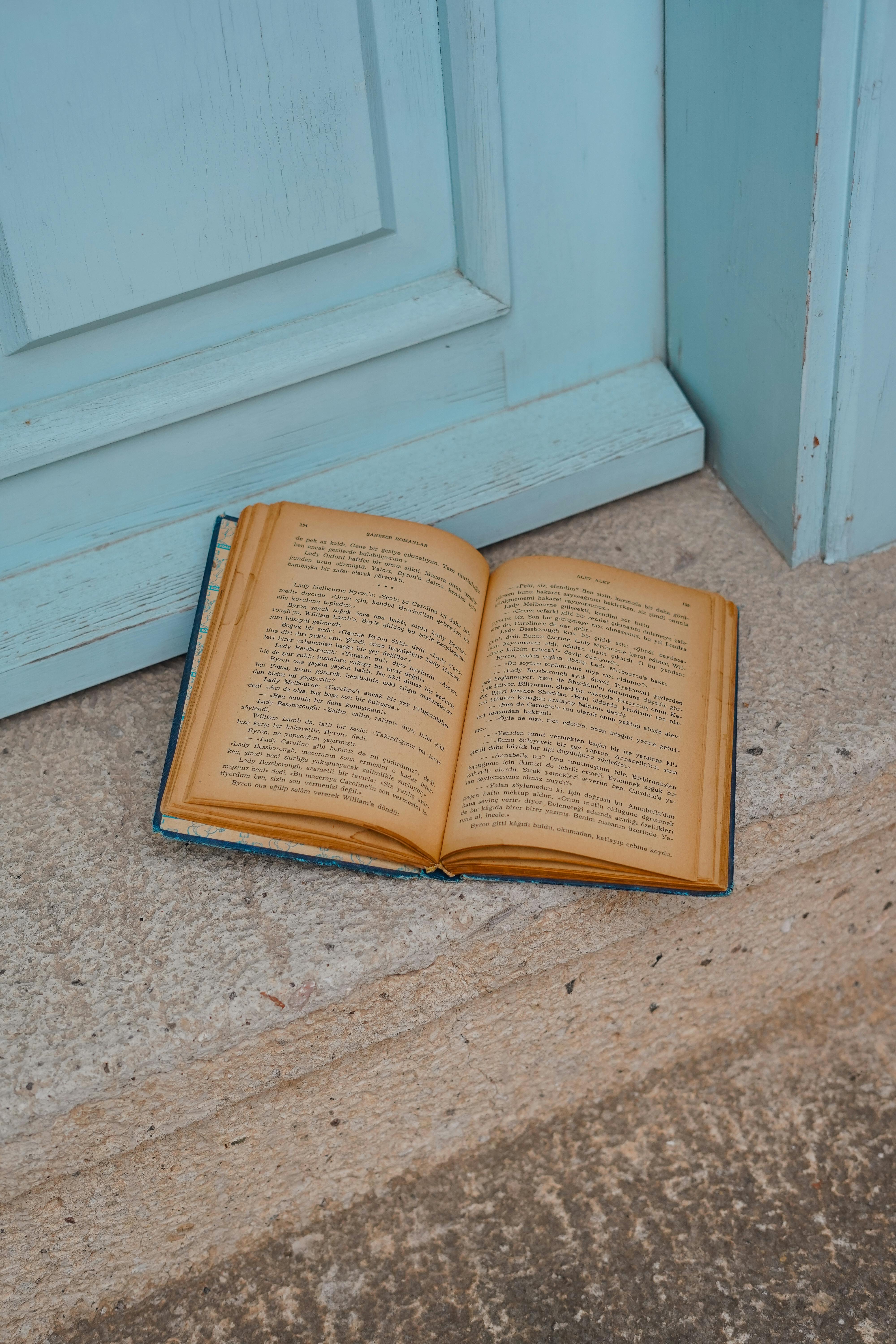 An open vintage book lies on a rustic wooden floor next to a blue door.