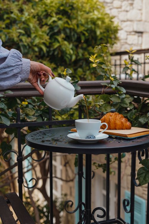 Free A scenic breakfast setting featuring tea pouring into a cup with a croissant on a balcony table. Stock Photo