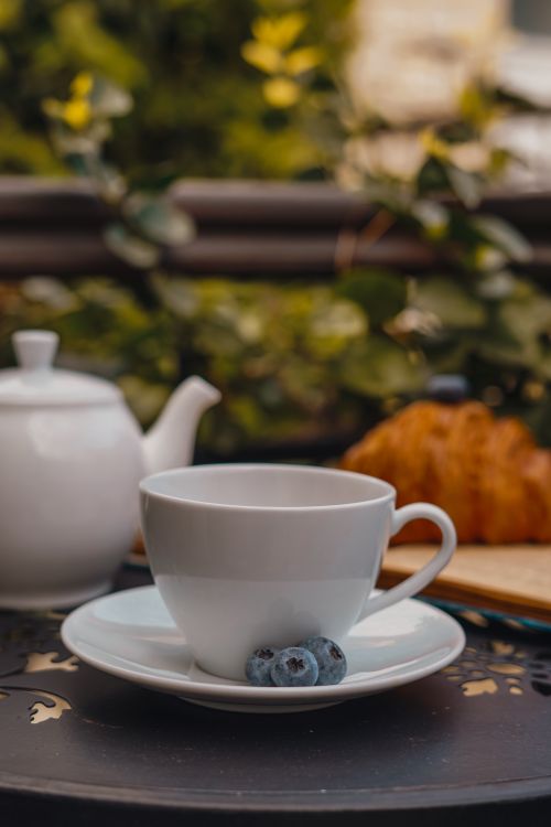 Free A serene morning scene with tea, blueberries, and a croissant outdoors. Stock Photo