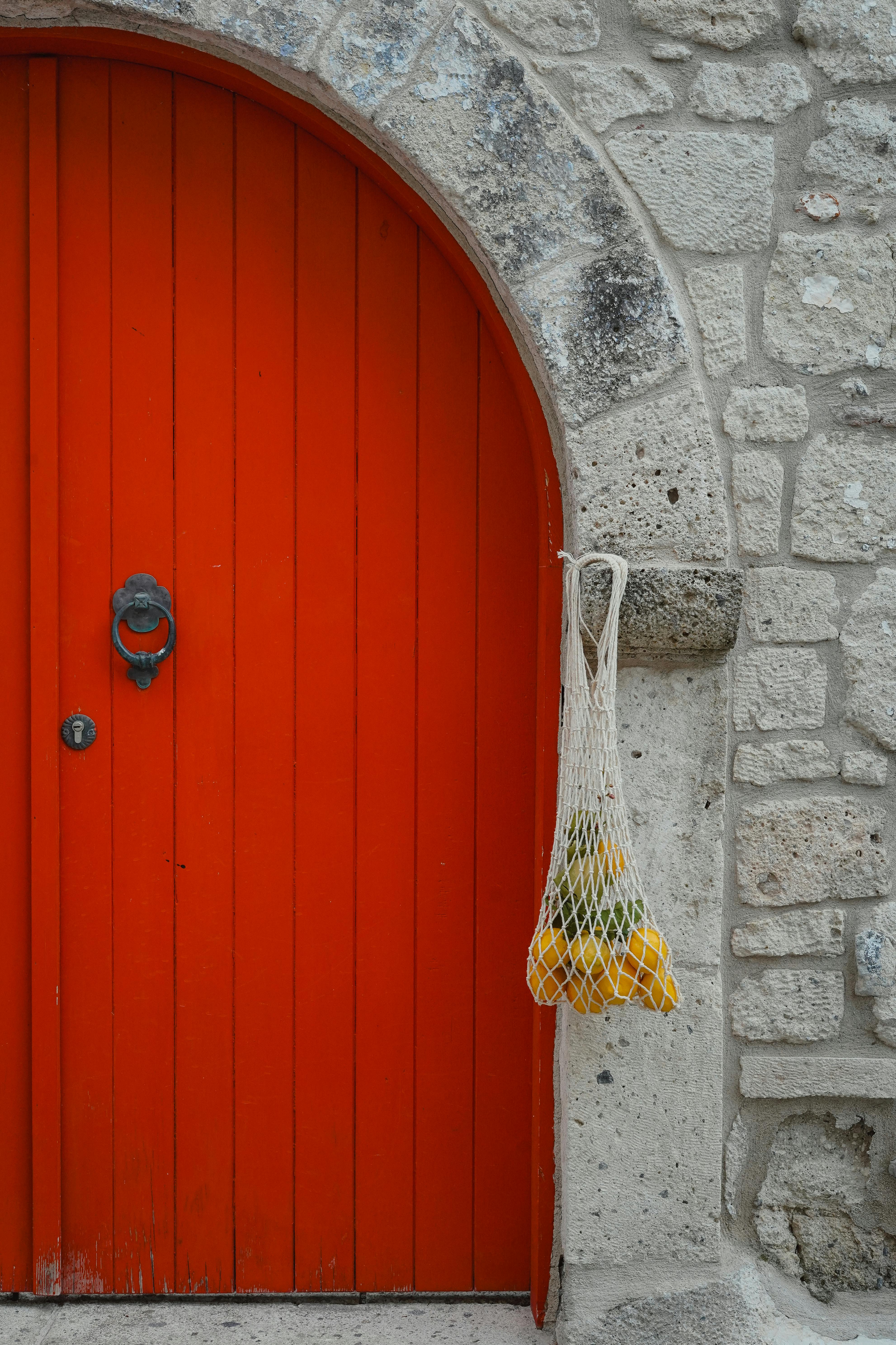 Colorful stone wall featuring a bright orange door and hanging mesh bag with lemons.
