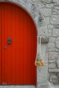 Colorful stone wall featuring a bright orange door and hanging mesh bag with lemons.