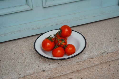 Free A collection of ripe cherry tomatoes in a vintage white bowl on a stone surface. Stock Photo