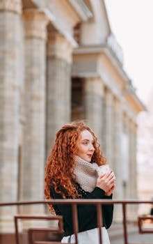 一位红发时尚的年轻女子在阳光明媚的城市环境中享受户外咖啡