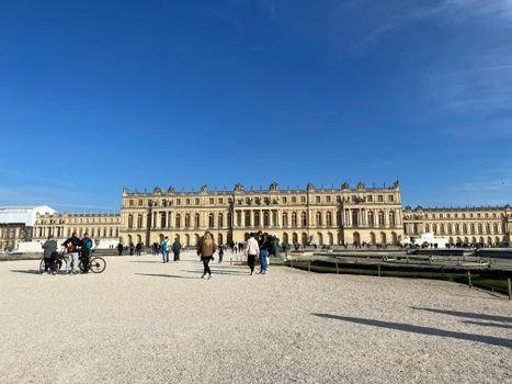 Visitors exploring the historic Palace of Versailles on a sunny day, showcasing its grandeur.