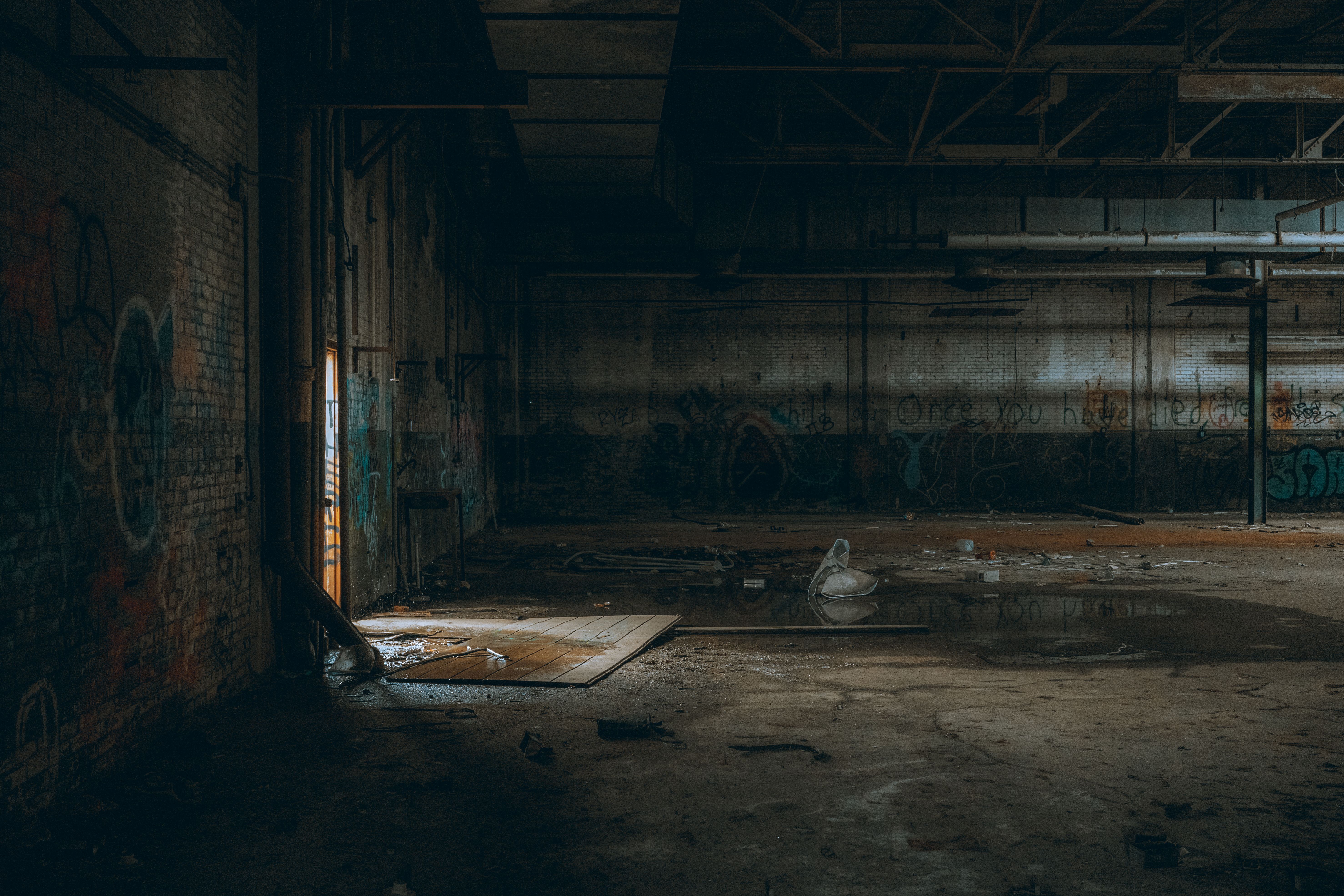 Dimly lit interior of an abandoned warehouse featuring graffiti and debris.