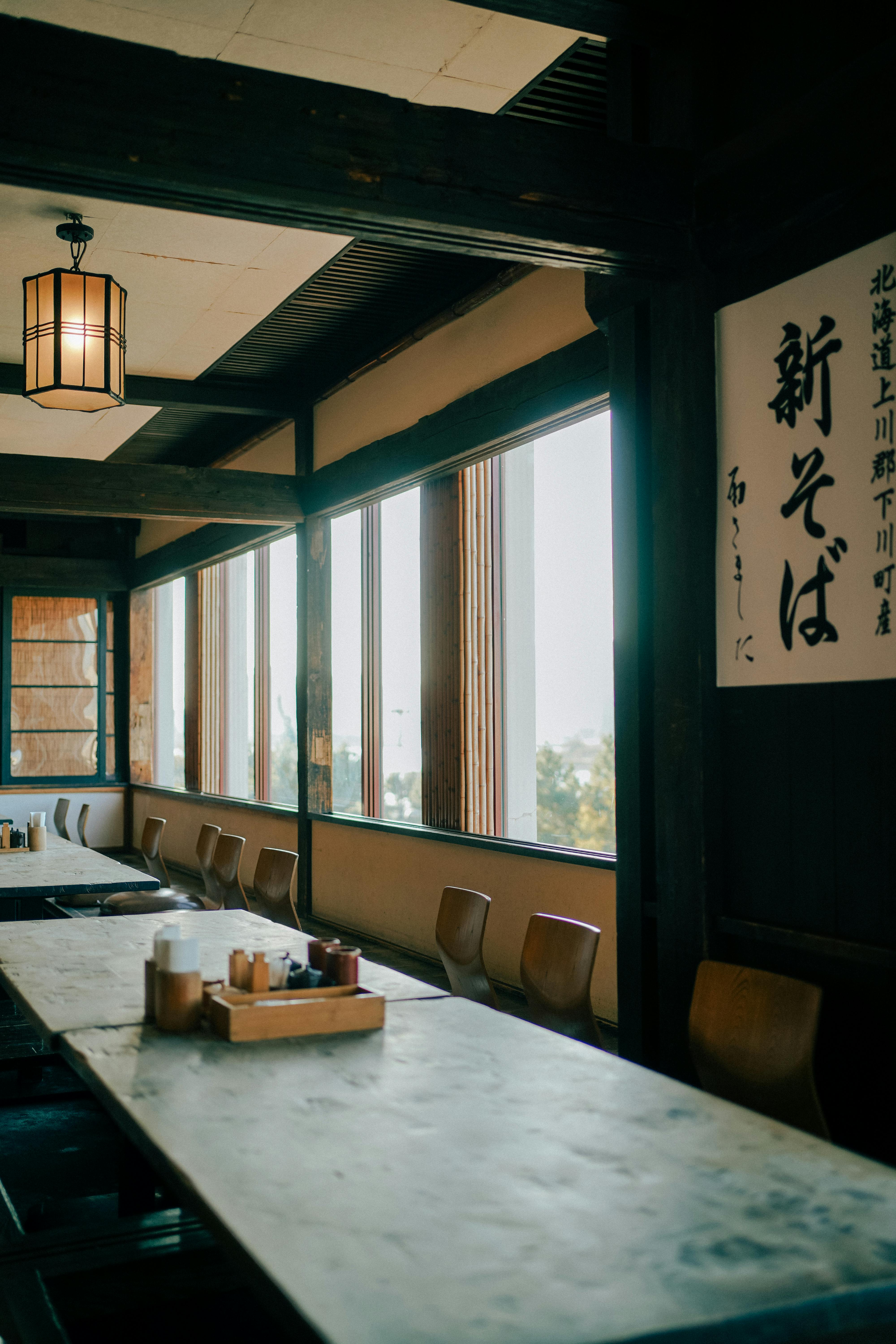 Cozy Japanese restaurant interior with wooden tables and traditional decor, illuminated by soft natural light.