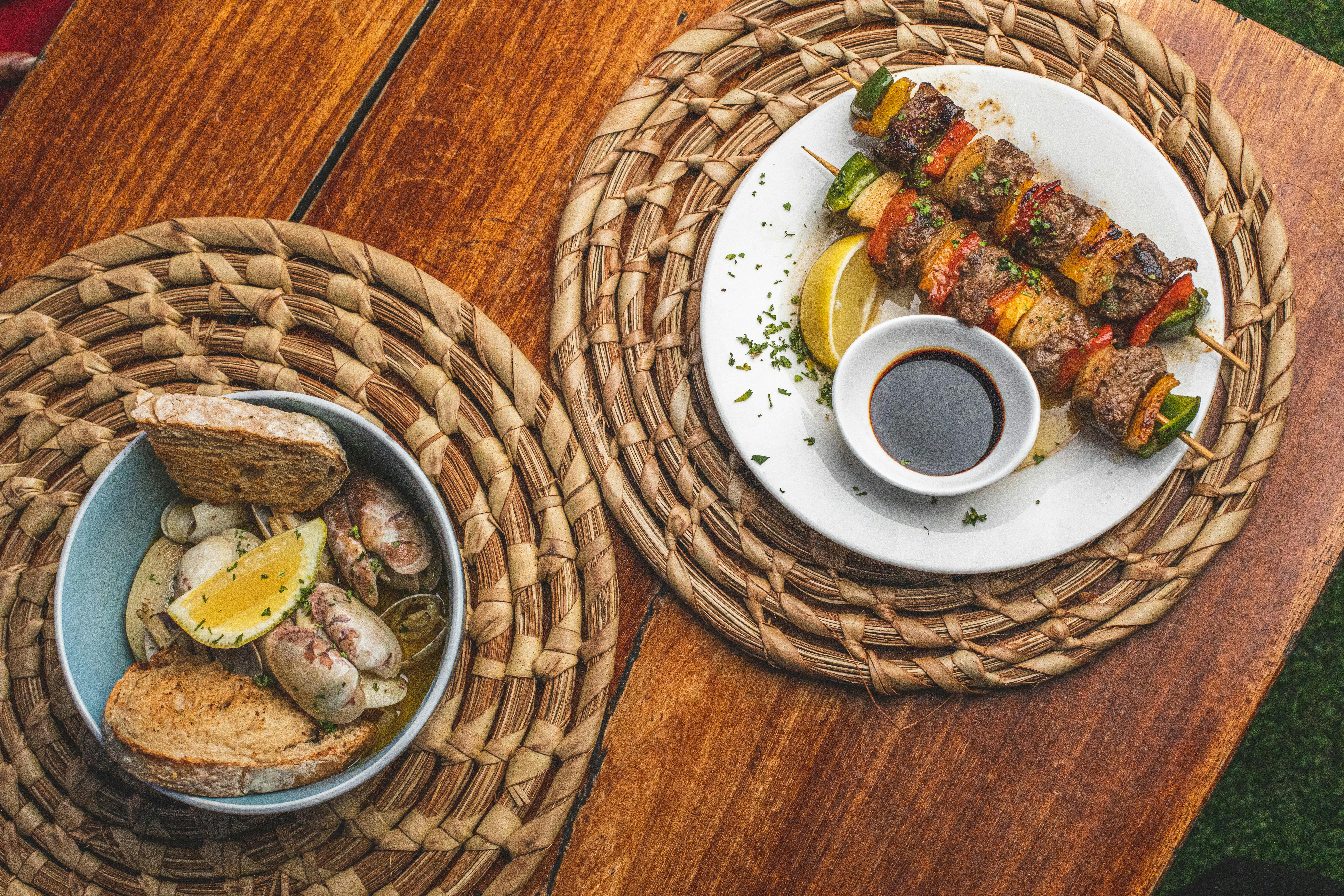 A delightful presentation of skewered kebabs and a seafood bowl with lemon garnishes on a woven mat.