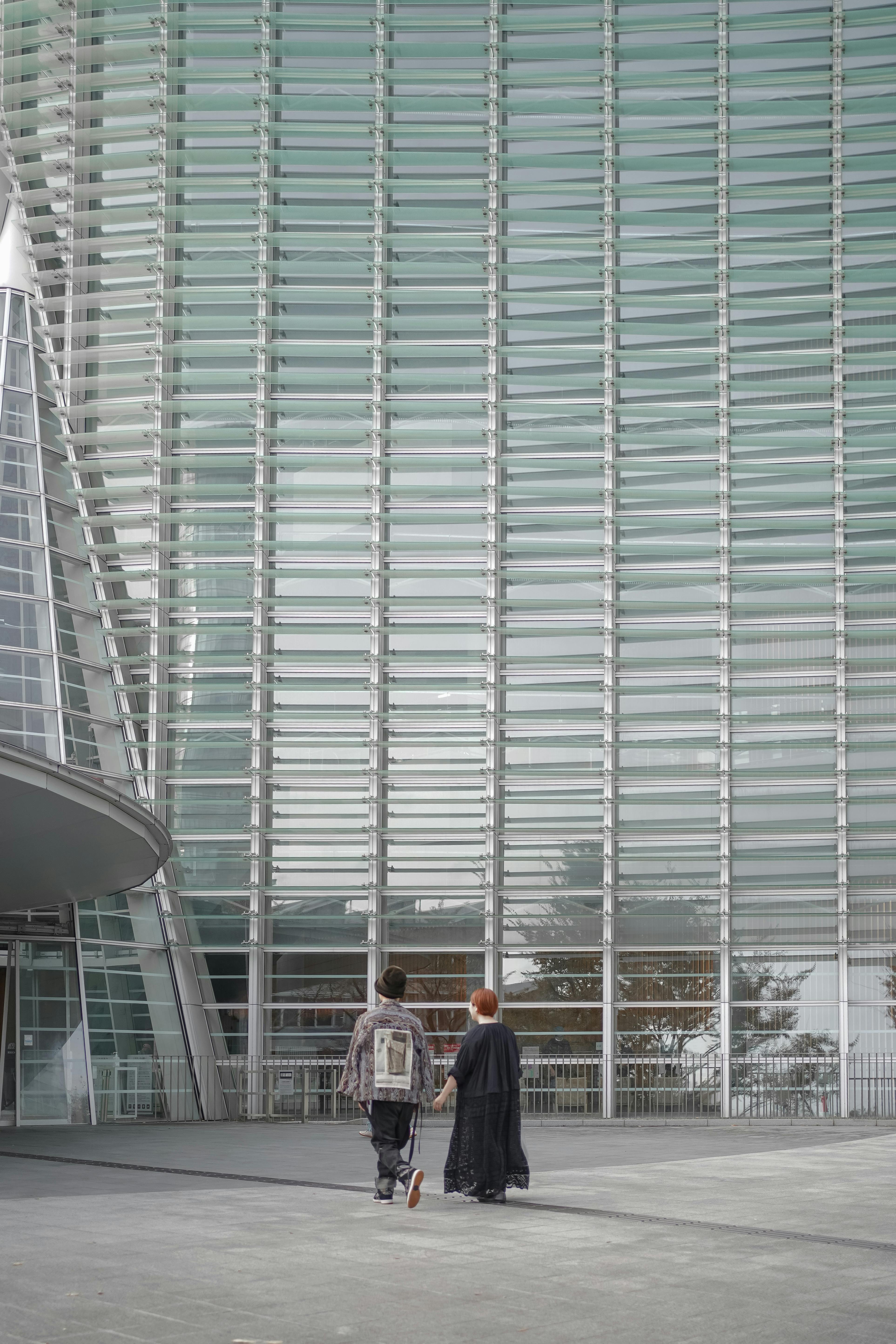 Two people walk near a modern architectural facade in Japan.