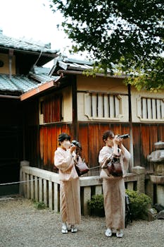 Two women in kimono capturing moments with cameras outside a traditional Japanese building.